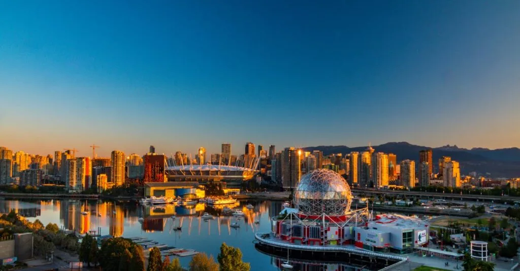 A panoramic view of Vancouver at sunrise, featuring the iconic Science World building, the BC Place Stadium, and a bustling downtown skyline reflected in the calm water.